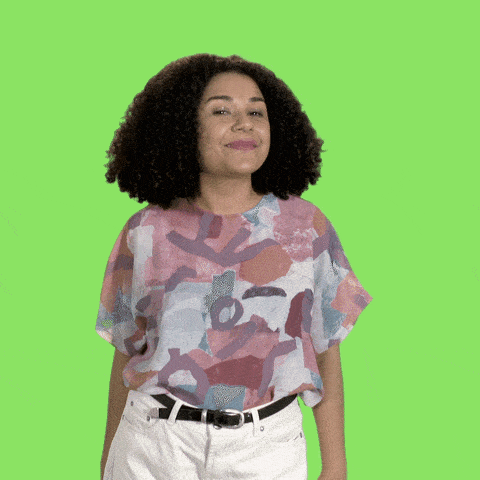 a woman standing in front of a green screen and she pulls her hands together to make a heart 
