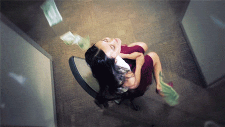 a woman spinning around on a chair with lots money falling on her in an office